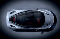 Overhead view of McLaren by Schiffer Publishing, Ltd.—a sleek silver car with a glass roof and visible red interior—photographed on a dark, spotlighted background.